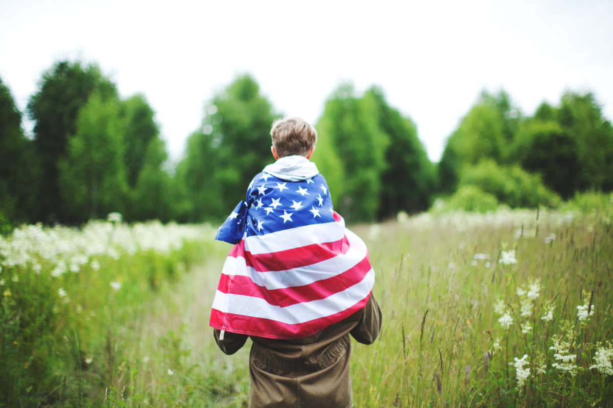 child sitting on parents shoulders with American flag draped over them